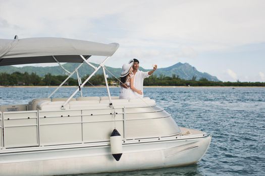 Young couple is traveling on a yacht in the Indian ocean. On the bow of the boat, a loving family takes selfie.