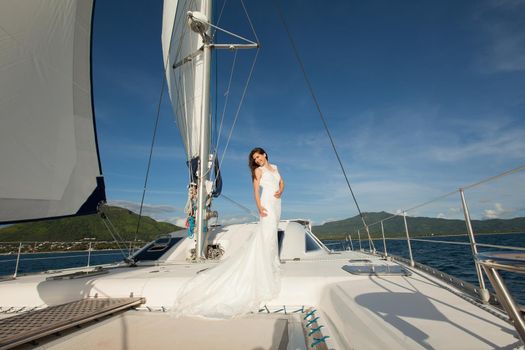 Happy bride on a yacht. White yacht with sail set goes along the island