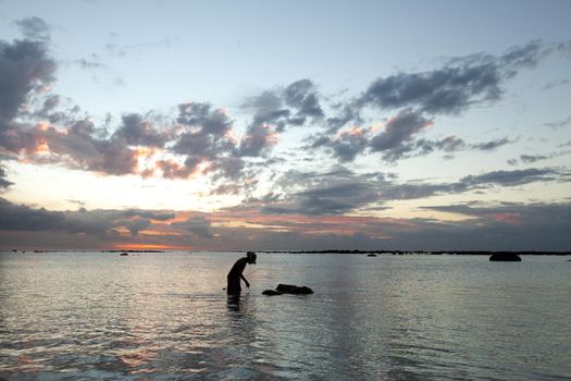 A fisherman catches a fish in the ocean at sunset.