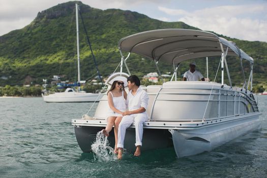 Young couple is sailing on a yacht in the Indian ocean. Man and woman sit on the edge of the yacht