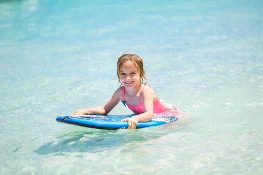 Little baby girl - young surfer with bodyboard has a fun on small ocean waves. Active family lifestyle