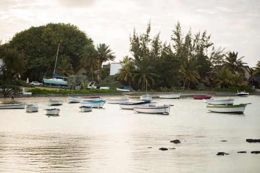 Yachts and fishing boats on the shore with black large stones with mountain range in the background