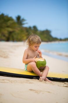 Happy funny little preschool kid boy drinking coconut juice on ocean beach.