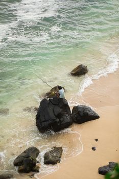 Fisherman is fishing in the black stones in the ocean.