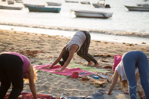 Women doing yoga exercises or supported pigeon pose on an empty beach of the Indian ocean in Mauritius