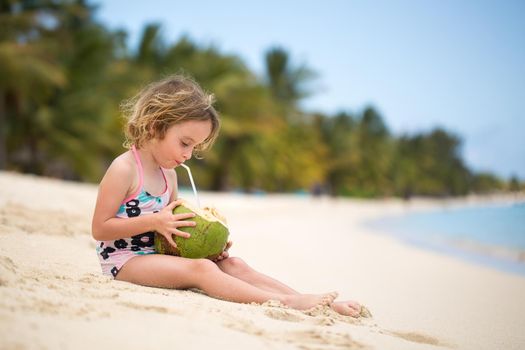 Little preschool kid girl drinking coconut juice on ocean beach.