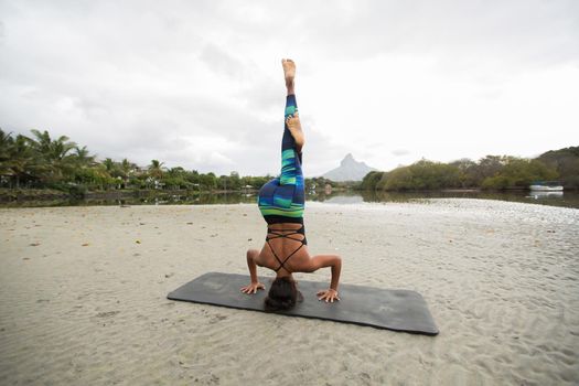 Young woman practices yoga on the shore of the Indian ocean in Mauritius and mountain in the background