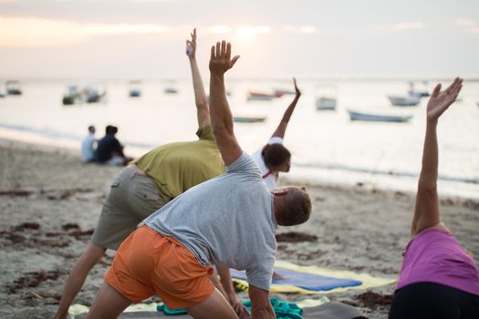 Women doing yoga exercises or supported pigeon pose on an empty beach of the Indian ocean in Mauritius