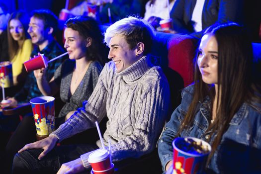 Friends sit and eat popcorn together while watching movies in a movie theater