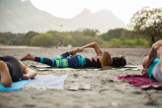 Women doing yoga exercises or supported pigeon pose on the background mountain on the empty beach of the Indian ocean in Mauritius