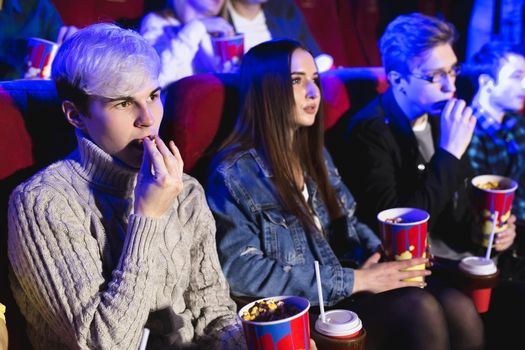 Young man eats popcorn in the cinema and watches a movie.