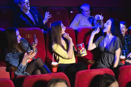 Cheerful group of friends in the cinema is having fun and throwing popcorn.