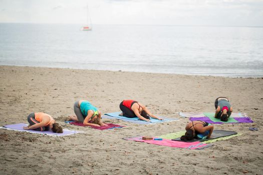 Women doing yoga exercises or supported pigeon pose on the background mountain on the empty beach of the Indian ocean in Mauritius