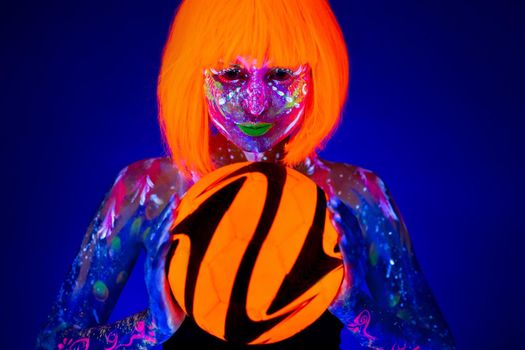 Woman in neon makeup holds a soccer ball in her hands. Concept of the world Cup. Fluorescent paint in UV light