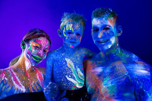 Family, mom, dad and son are painted in UV powder. Futuristic body art, fluorescent paints glows in neon light