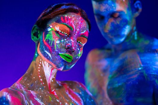 Portrait of a beefy man and woman painted in ultraviolet powder. Body art glowing in ultraviolet light