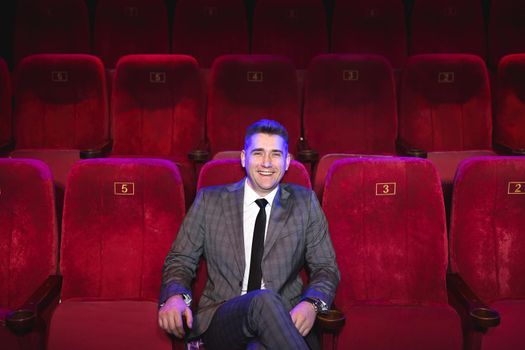 Portrait of a young handsome man alone in a movie theater in a business suit