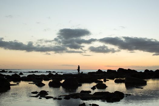 A fisherman is fishing in the black stones in the ocean.