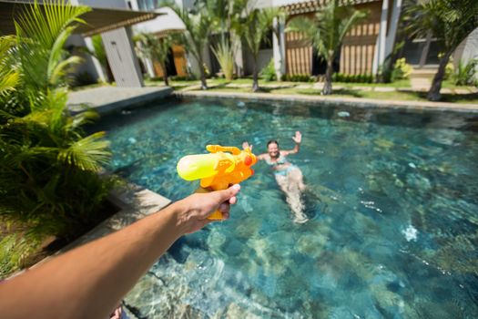 Man fires a water gun into a woman, while having fun in the pool.