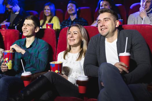 Friends sit and eat popcorn together while watching movies in a movie theater