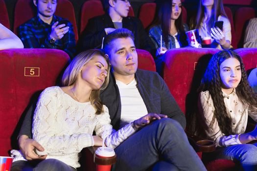 Young people watching a boring movie at the cinema, girl is sleeping