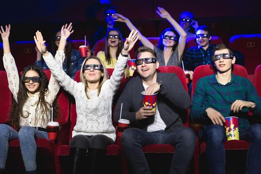 Friends in the cinema watch a funny movie with 3D glasses, laugh, have fun.