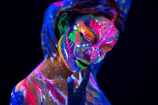 Fashion model woman in neon light, portrait of beautiful model girl with fluorescent make-up, Body Art design of female disco dancer posing in UV, painted face, colorful make up, over black background