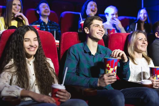 Friends sit and eat popcorn together while watching movies in a movie theater