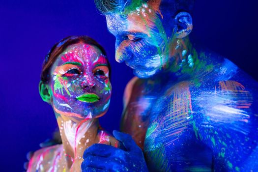 Portrait of a beefy man and woman painted in ultraviolet powder. Body art glowing in ultraviolet light