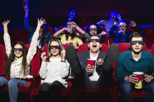 Friends in the cinema watch a funny movie with 3D glasses, laugh, have fun.