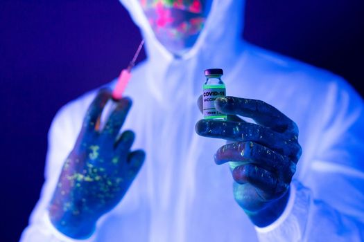 Doctor in ultraviolet neon light is holding COVID-19, oronavirus vaccine and syringe using for prevent infection. Medicine and Healthcare concept