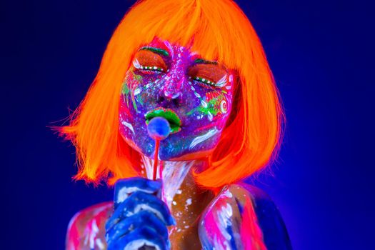 Fashion model woman licks sweet candy in neon light, disco night club. Beautiful model girl colorful bright fluorescent makeup