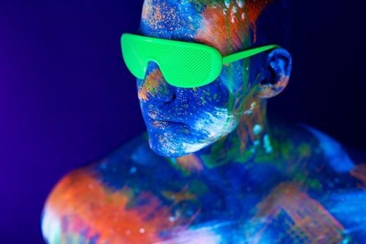 Young man shouts. Fluorescent paint on face and muscular torso, in studio shot with UV light