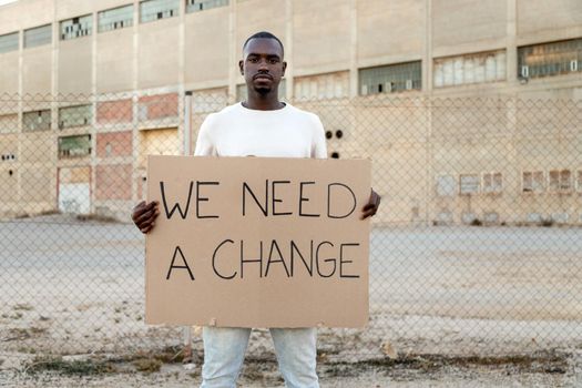 Young African American man looking at camera holding a we need a change banner protesting for black lives matter movement. Copy space. Social movement activist concept.