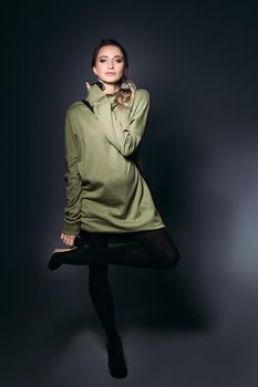 Portrait of elegant and fashionable pregnant brunette woman posing at dark studio. Stylish woman wearing in khaki dress, holding pregnant belly, looking at side. Concept of pregnancy.