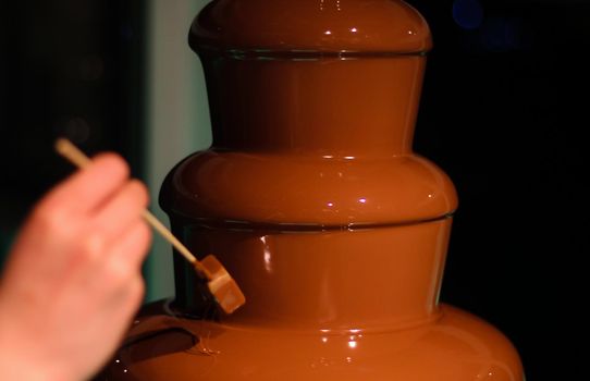 Person dipping a block of British fudge on a skewer into a chocolate fountain fondue, at a wedding in Hampshire, UK. High quality photo.