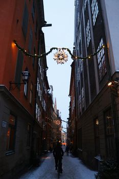 Christmas decorations, cyclist and lights in a snowy street in the centre of Stockholm, 'Gamla Stan' in winter, Sweden. High quality photo.