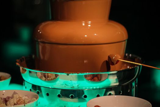 Strawberry skewer being dipped into a chocolate fountain fondue, at a wedding in Hampshire, UK. High quality photo.