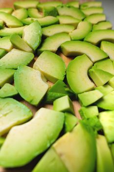 Pieces of juicy sliced avocado lie textured on a wooden cutting board. Delicious vegan background.