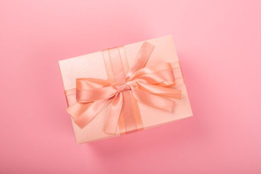 Valentines Day gift in a box wrapped in striped paper and tied with silk ribbon bow on pink background with copy space for text