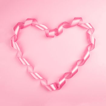 Valentine day background with pink curly satin ribbon in heart shape on paper on with copy space for text