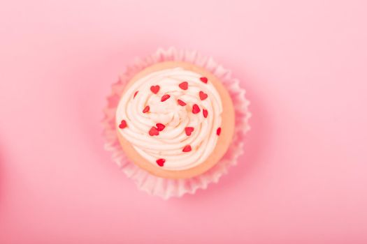 Valentine day love cupcake decorated with cream and hearts on pink background with copy space for text top view