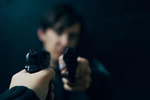 Close-up of man's hand with gun pointed at criminal with revolver. Shootout of two thieves or murderers. Firearms for attack or defense.