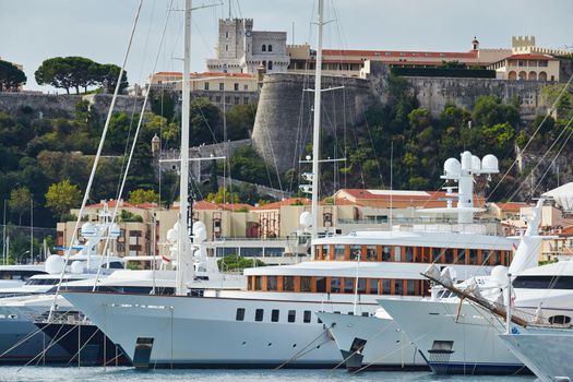 Monaco, Monte-Carlo, a lot of large motor yachts are parked side by side in the port, with huge fenders between them to avoid collision at sunny day, mooring ropes go into the azure water. High quality photo