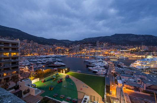 Aerial view of port Hercules in Monaco - Monte-Carlo at dusk, a lot of yachts and boats are moored in marina, cityscape with night illumination, magic reflection on water, mountain, mediterranean sea. High quality photo