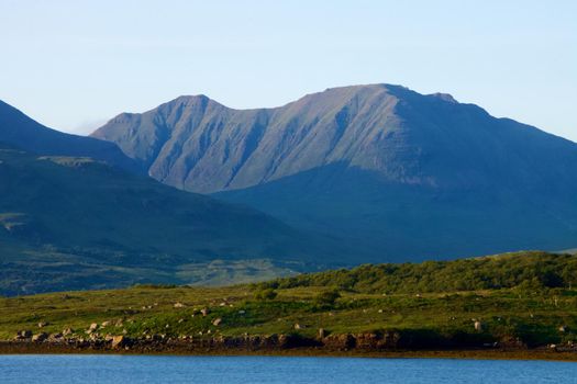 View of a lake in the Scottish Highlands on part of the north coast 500 route with sun-drenched and shadowed mountains in the background. Taken with Canon EOS 90D