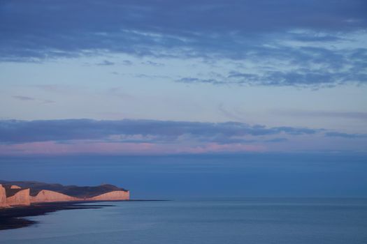 Dramatic view of the Seven Sisters coastline, sea and clouds in sky at sunset with blue and pink colours. Taken in summer, England, UK on Canon EOS 90D.