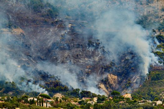 Fire in the forest mountain in the Italian town of Ventimiglia, all the mountains in the smoke, the villa is on fire, the fire service aircraft extinguish a fire. High quality photo