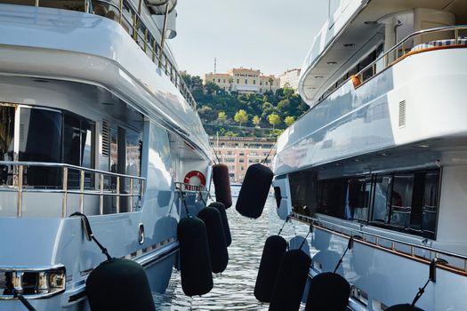 Monaco, Monte-Carlo, two large motor yachts are parked side by side in the port, with huge fenders between them to avoid collision at sunny day, mooring ropes go into the azure water. High quality photo