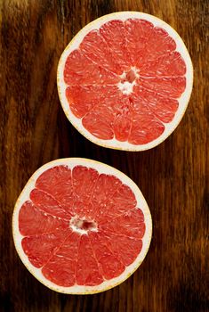 Two half of red grapefruit, bright circles on a dark wooden background. citrus fruits, vertical